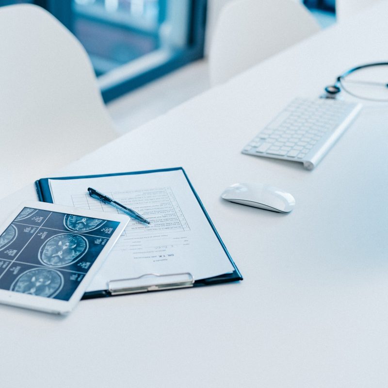 Closeup shot of a clipboard and a digital tablet with brain scans on a desk in a doctor's office